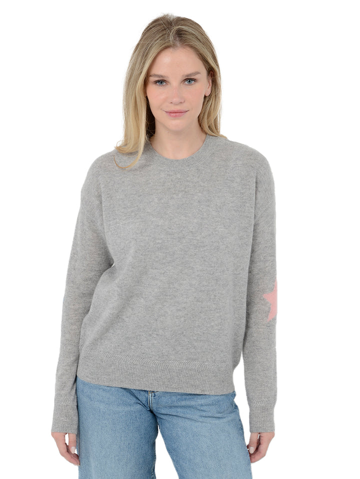 Front facing shot of model wearing Rowan in heather gray. The sweater is straight fit and made of cashmere and silk. The pullover has colorful stars on the back of the arm.