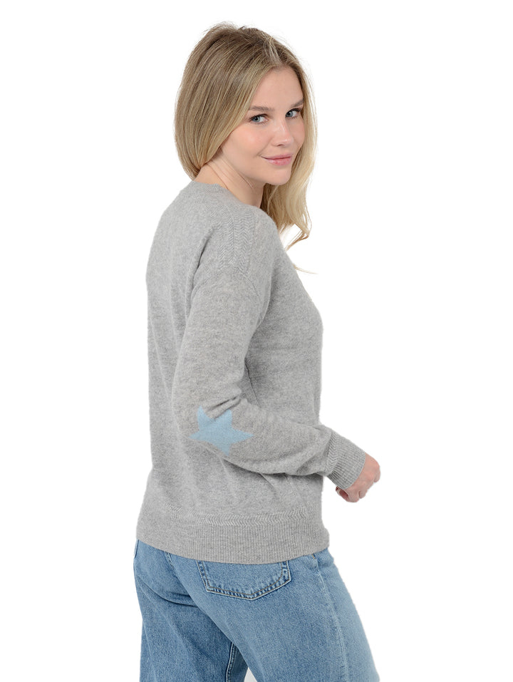 3/4 back view of model wearing Rowan in heather gray. The sweater is straight fit and made of cashmere and silk. The pullover has colorful stars on the back of the arm.