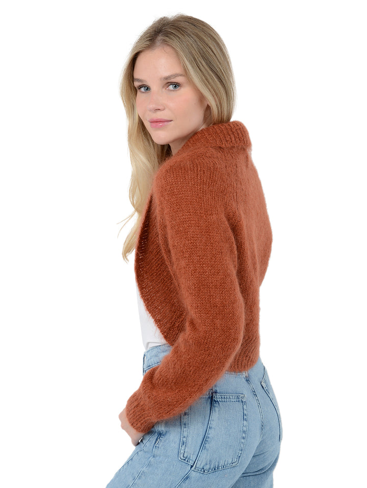 Side view of model wearing Odi in ginger orange. The sweater is relaxed and made of mohair and wool. The sweater is a shrug with a ribbed-knit shawl lapel.