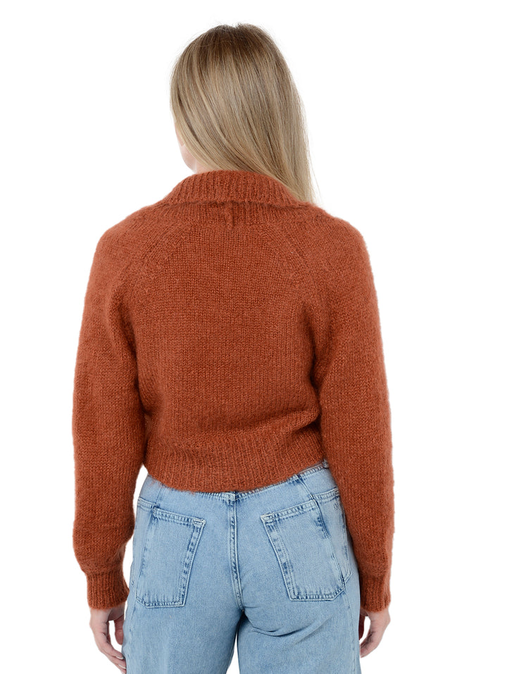 Back facing shot of model wearing Odi in ginger orange. The sweater is relaxed and made of mohair and wool. The sweater is a shrug with a ribbed-knit shawl lapel.