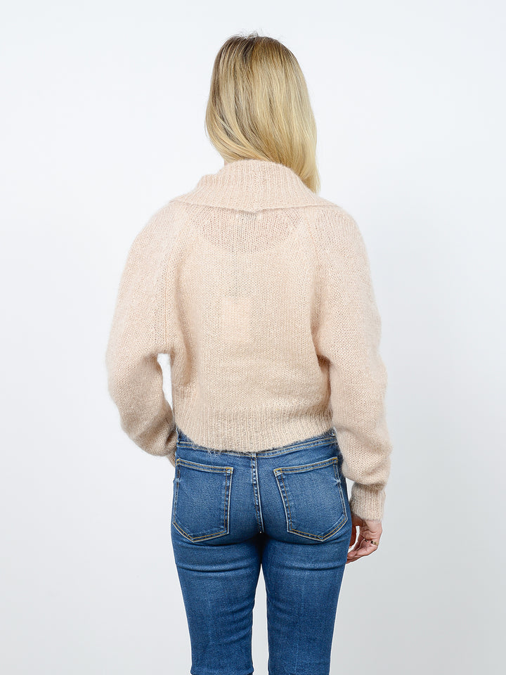 Back facing shot of model wearing Odi in latte cream. The sweater is relaxed and made of mohair and wool. The sweater is a shrug with a ribbed-knit shawl lapel.