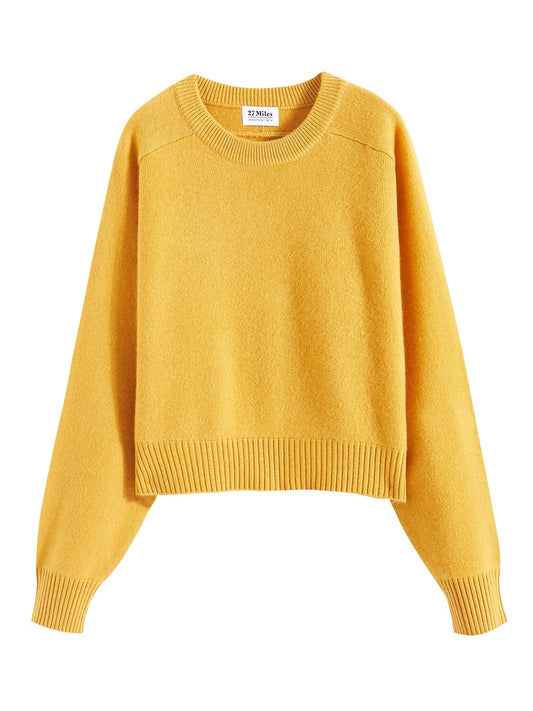 Flatlay photo of Iliana in marigold yellow. The sweater is cropped and oversized and made of 100% cashmere. The sweater also sports saddle sleeves and a crewneck with tall cuffs and bottom trims.