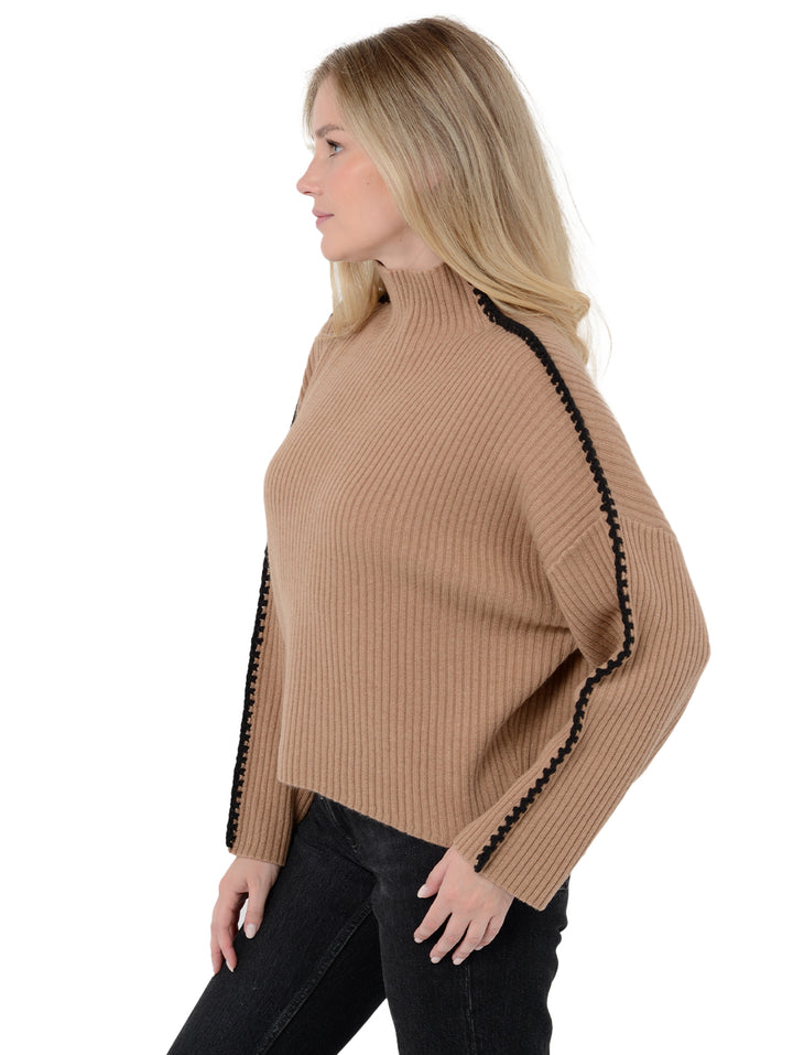 Side view of model wearing Marullo in camel brown. The sweater is oversized and made of wool and cashmere. The sweater is a mock neck with crochet-like embroidery along the sleeves and shoulders.