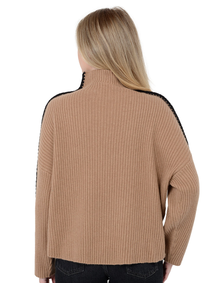 Back facing shot of model wearing Marullo in camel brown. The sweater is oversized and made of wool and cashmere. The sweater is a mock neck with crochet-like embroidery along the sleeves and shoulders.