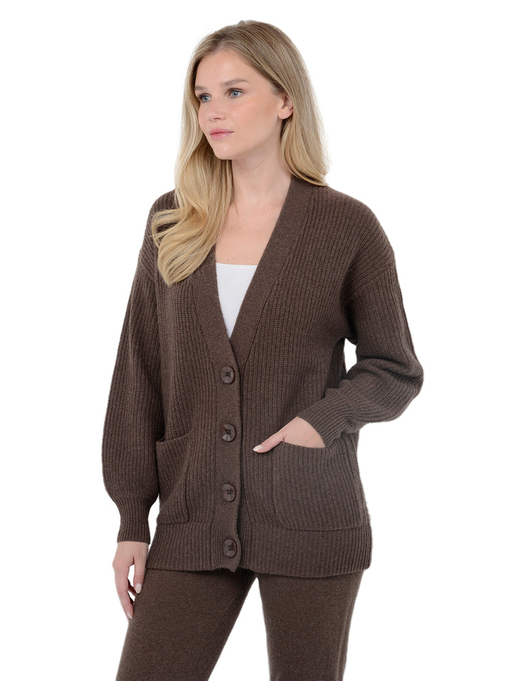 3/4 view of model wearing Kamira in cocoa brown. The sweater is oversized and made of cashmere and recycled cashmere. The style is a button-up cardigan with patch pockets.