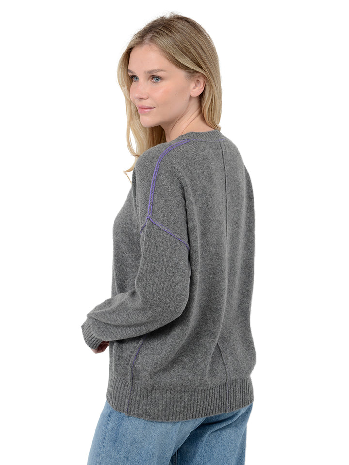 Side view of model wearing Venise in gravel grey. The sweater is oversized and made of cashmere and recycled cashmere. The sweater is a crewneck pullover with decorative reversed seams.