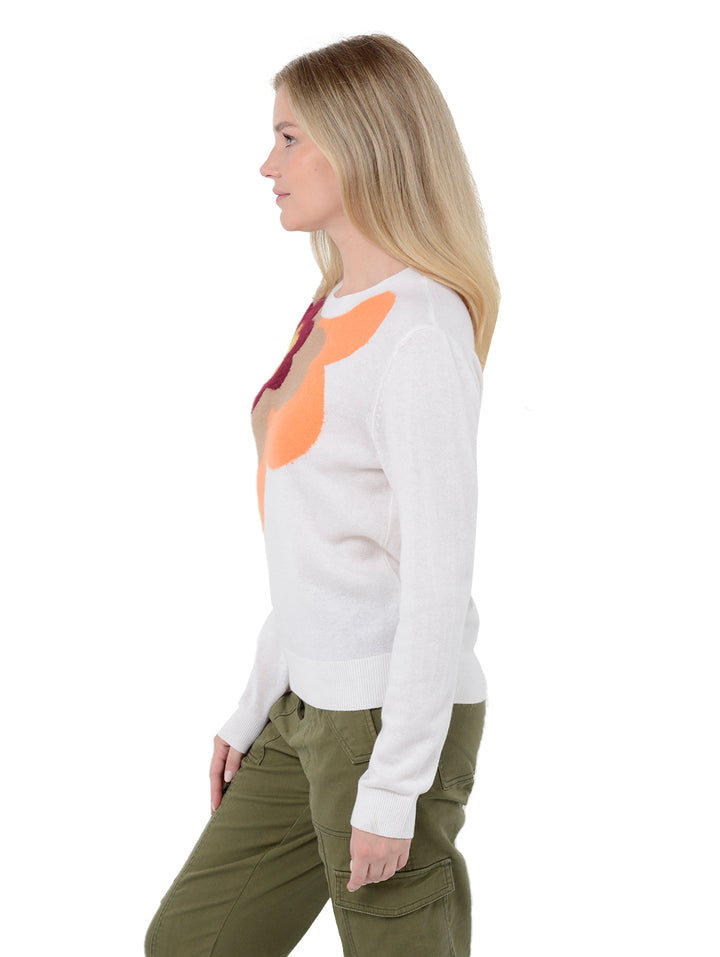 Side view shot of model wearing Alston in chalk white. The sweater is straight fit and made of cashmere, wool, and silk. The sweater is a crewneck pullover and has a large retro flower intarsia artwork.