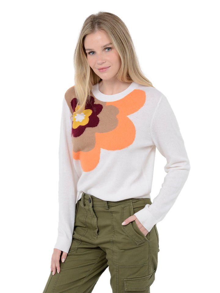 3/4 front facing shot of model wearing Alston in chalk white. The sweater is straight fit and made of cashmere, wool, and silk. The sweater is a crewneck pullover and has a large retro flower intarsia artwork.
