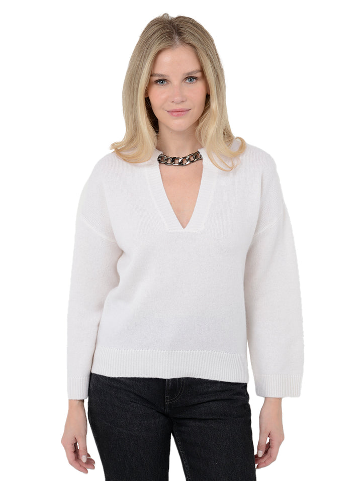 Front facing shot of model wearing Audrina in cloud white. The sweater is relaxed and made of 100% cashmere. The sweater also features a v-neck, drop shoulder, and silver chain trim across neckline.