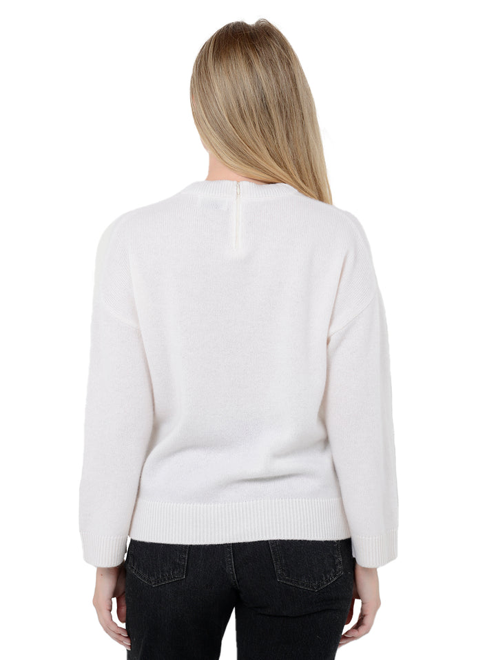 Back facing shot of model wearing Audrina in cloud white. The sweater is relaxed and made of 100% cashmere. The sweater also features a v-neck, drop shoulder, and invisible zipper at center back neck.