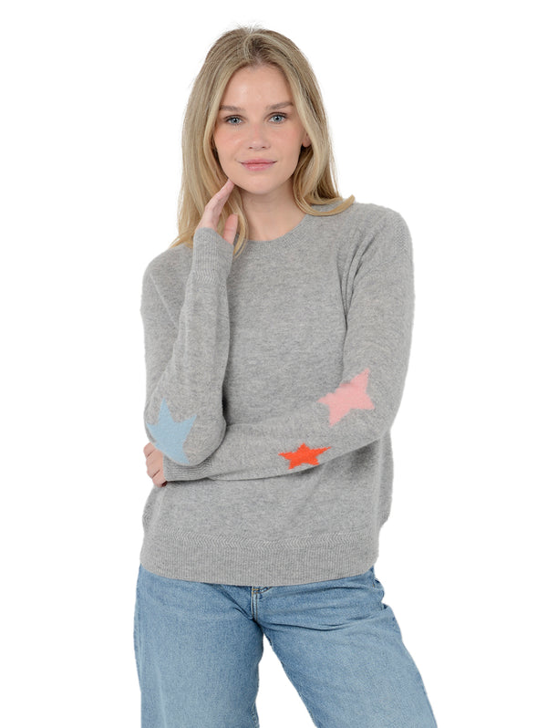 Alternate front facing shot of model wearing Rowan in heather gray. The sweater is straight fit and made of cashmere and silk. The pullover has colorful stars on the back of the arm. The model has her arms crossed and one hand touching her face.