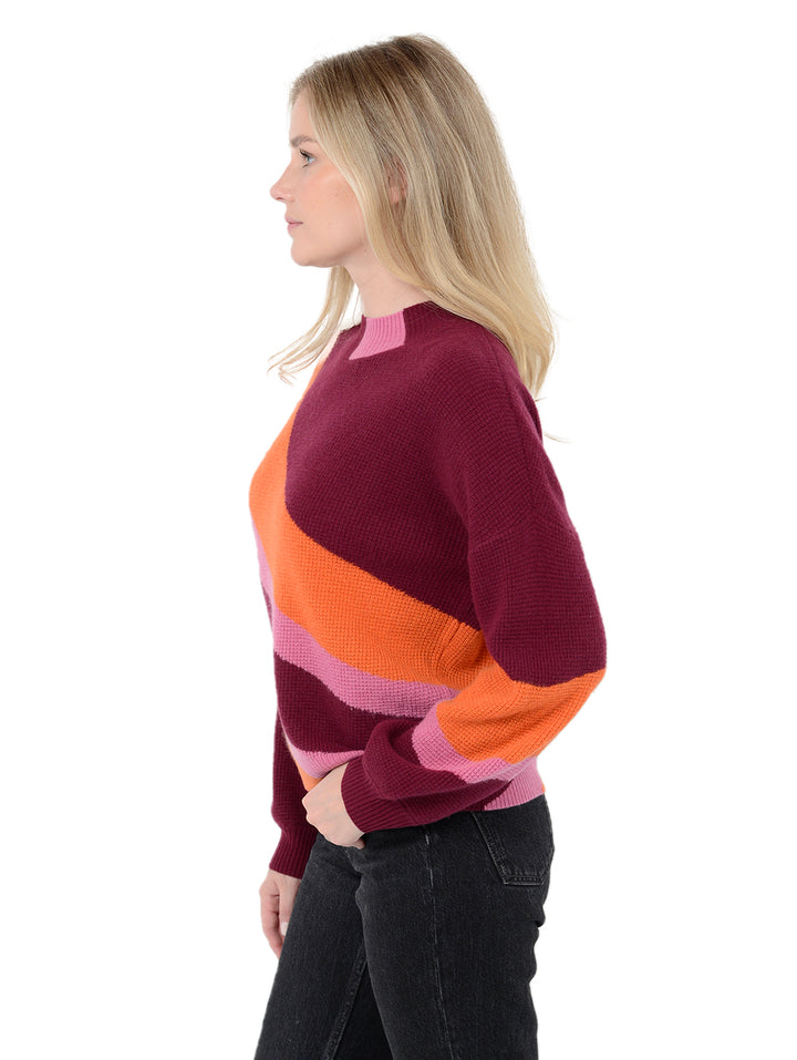 Side view of model wearing Norton in pinot burgundy. The sweater is oversized and made of 70% wool and 30% cashmere. The sweater is a mockneck and features diagonal stripes.
