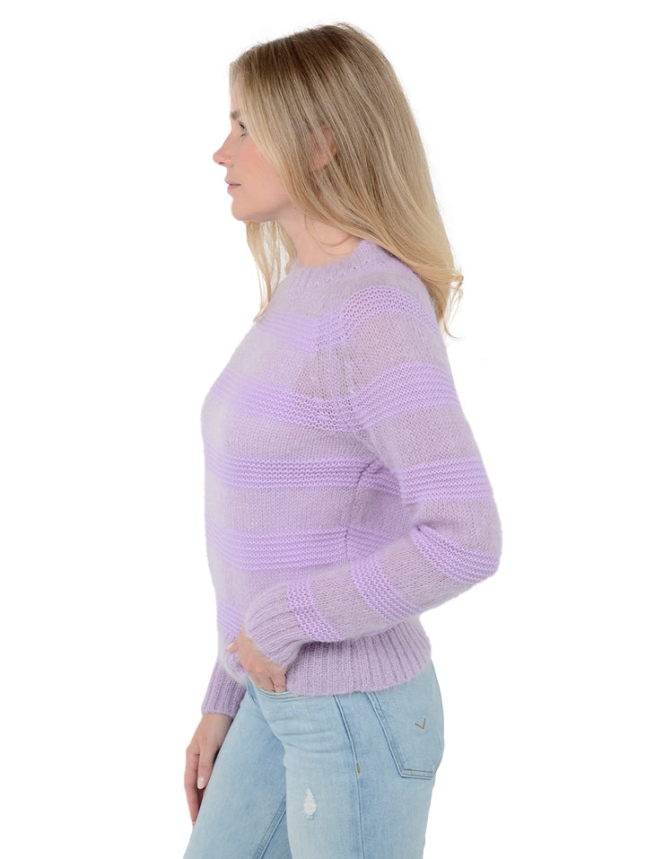 Side view of model wearing Soledad in lavender purple. The sweater is relaxed and made of wool and mohair with cashmere and wool contrast. The sweater is fuzzy with horizontal stripes.