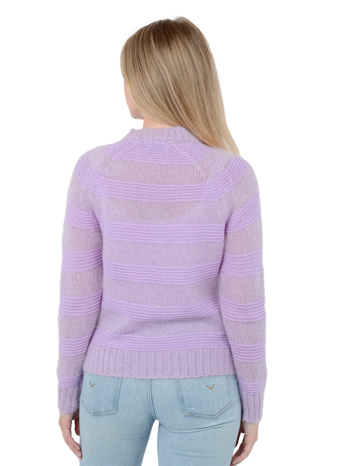 Back facing shot of model wearing Soledad in lavender purple. The sweater is relaxed and made of wool and mohair with cashmere and wool contrast. The sweater is fuzzy with horizontal stripes.