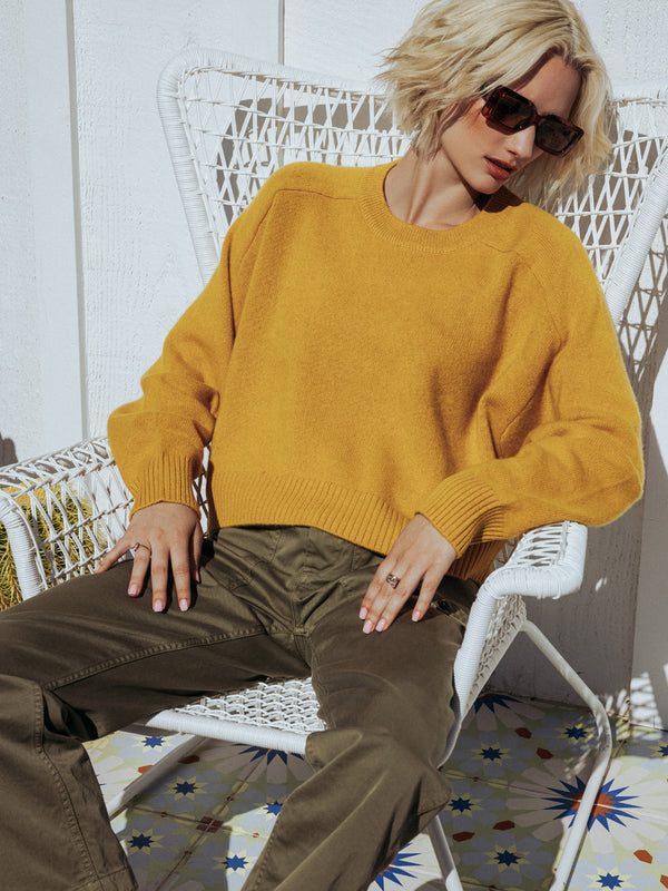 Editorial photo of model wearing Iliana in marigold yellow. The sweater is cropped and oversized and made of 100% cashmere. The sweater also sports saddle sleeves and a crewneck with tall cuffs and bottom trims.
