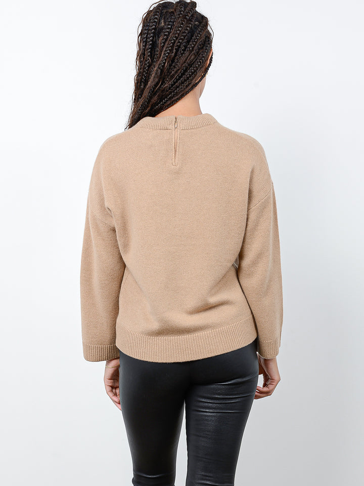 Back facing shot of model wearing Audrina in camel. The sweater is relaxed and made of 100% cashmere. The sweater also features a v-neck, drop shoulder, and invisible zipper at center back neck.