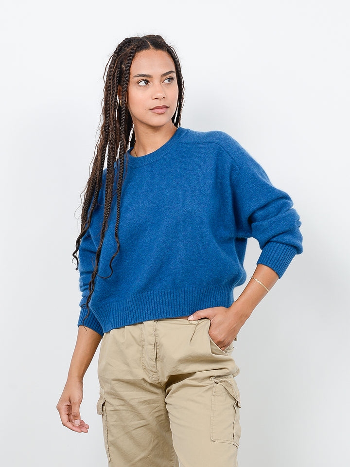 Front facing shot of model wearing Iliana in marine blue. The sweater is cropped and oversized and made of 100% cashmere. The sweater also sports saddle sleeves and a crewneck with tall cuffs and bottom trims.