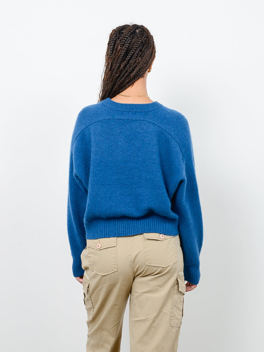 Back facing shot of model wearing Iliana in marine blue. The sweater is cropped and oversized and made of 100% cashmere. The sweater also sports saddle sleeves and a crewneck with tall cuffs and bottom trims.