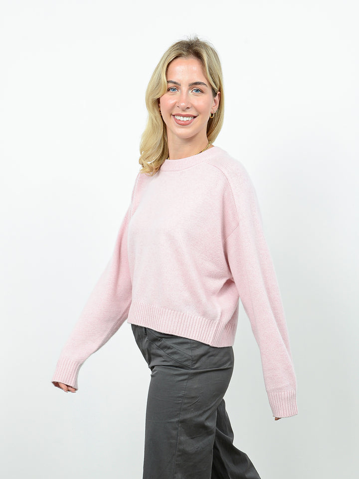 Side view shot of model wearing Iliana in petal pink. The sweater is oversized and cropped and made of 100% cashmere. The sweater also sports a saddle sleeve and crewneck.