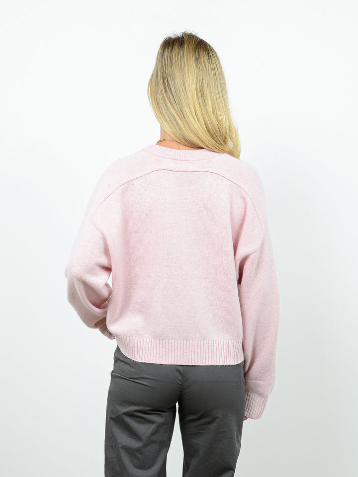 Back facing shot of model wearing Iliana in petal pink. The sweater is oversized and cropped and made of 100% cashmere. The sweater also sports a saddle sleeve and crewneck.
