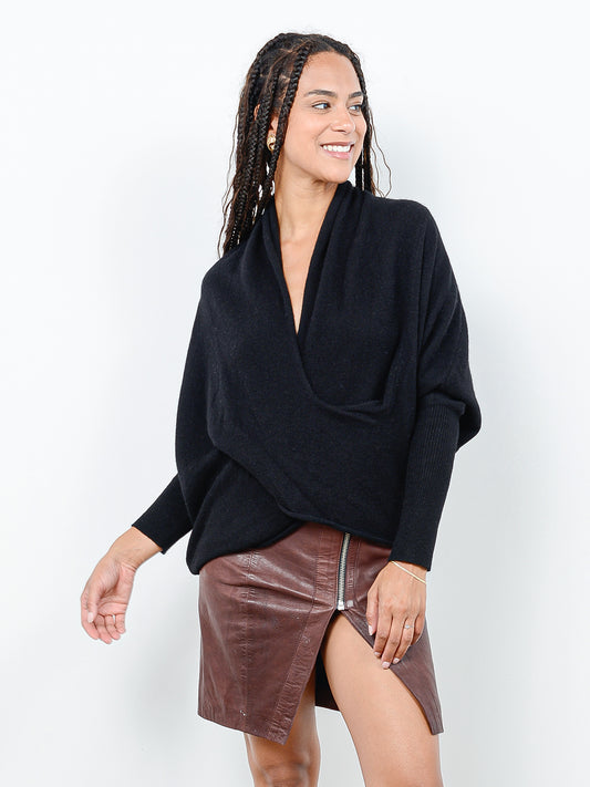 Front facing shot of model wearing Kirra in black. The sweater is oversized and made of cashmere and recycled cashmere. The sweater has a draped cowl neck with dolman sleeves that are fitted at the forearm.