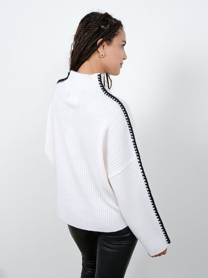 Back facing shot of model wearing Marullo in cloud white. The sweater is oversized and made of wool and cashmere. The sweater is a mock neck with crochet-like embroidery along the sleeves and shoulders.