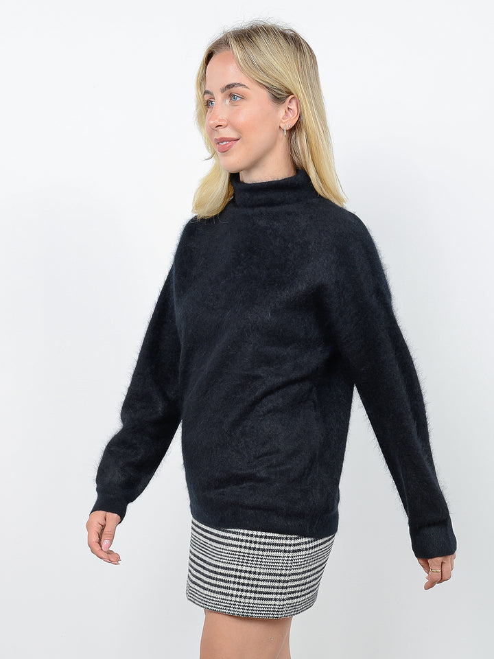 Side view of model wearing Morgan in black. The sweater is oversized and made of 100% cashmere. The sweater is a fuzzy turtleneck pullover.