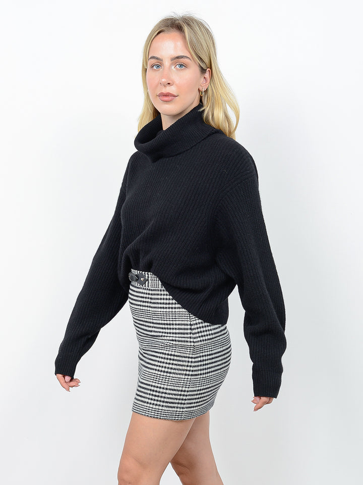 Side view of model wearing Naia in black. The sweater is oversized and cropped and made of cashmere and recycled cashmere. The sweater is a ribbed knit turtleneck.