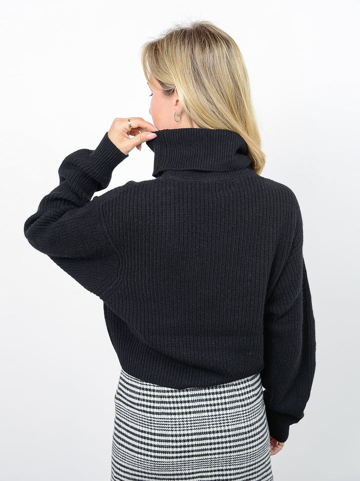 Back facing shot of model wearing Naia in black. The sweater is oversized and cropped and made of cashmere and recycled cashmere. The sweater is a ribbed knit turtleneck.