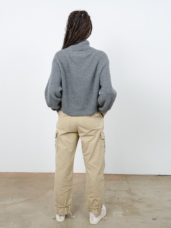 Back facing shot of model wearing Naia in gravel gray. The sweater is oversized and cropped and made of cashmere and recycled cashmere. The sweater is a ribbed knit turtleneck.