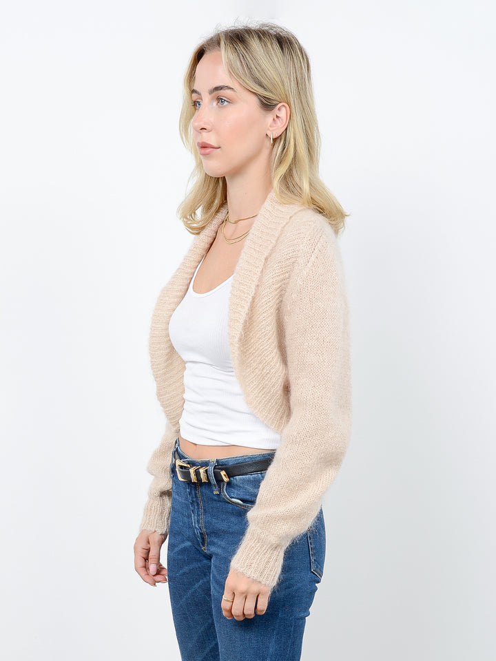 Side view of model wearing Odi in latte cream. The sweater is relaxed and made of mohair and wool. The sweater is a shrug with a ribbed-knit shawl lapel.