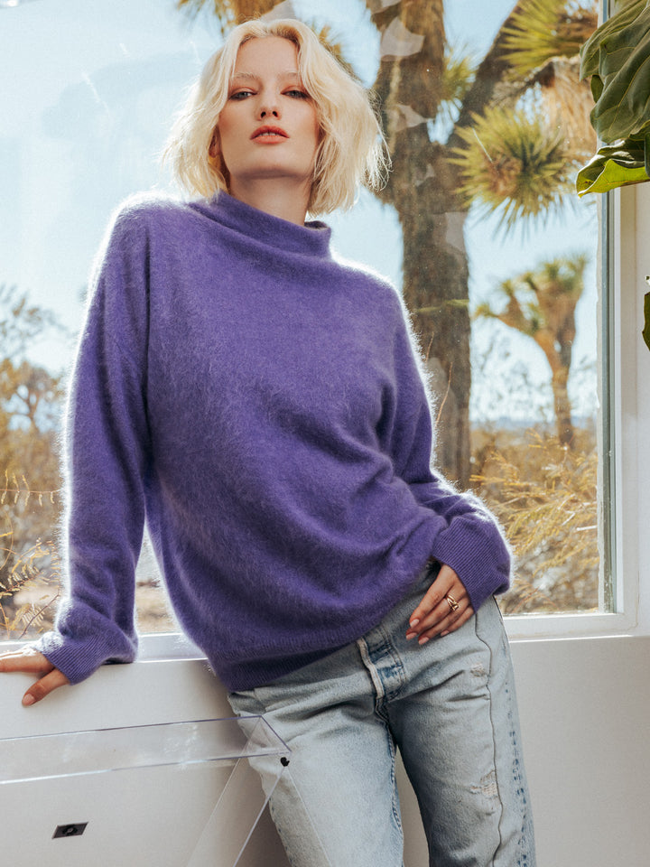 Editorial photo of model wearing oversized and fuzzy Morgan sweater. She is leaned against a window overlooking Joshua Tree.